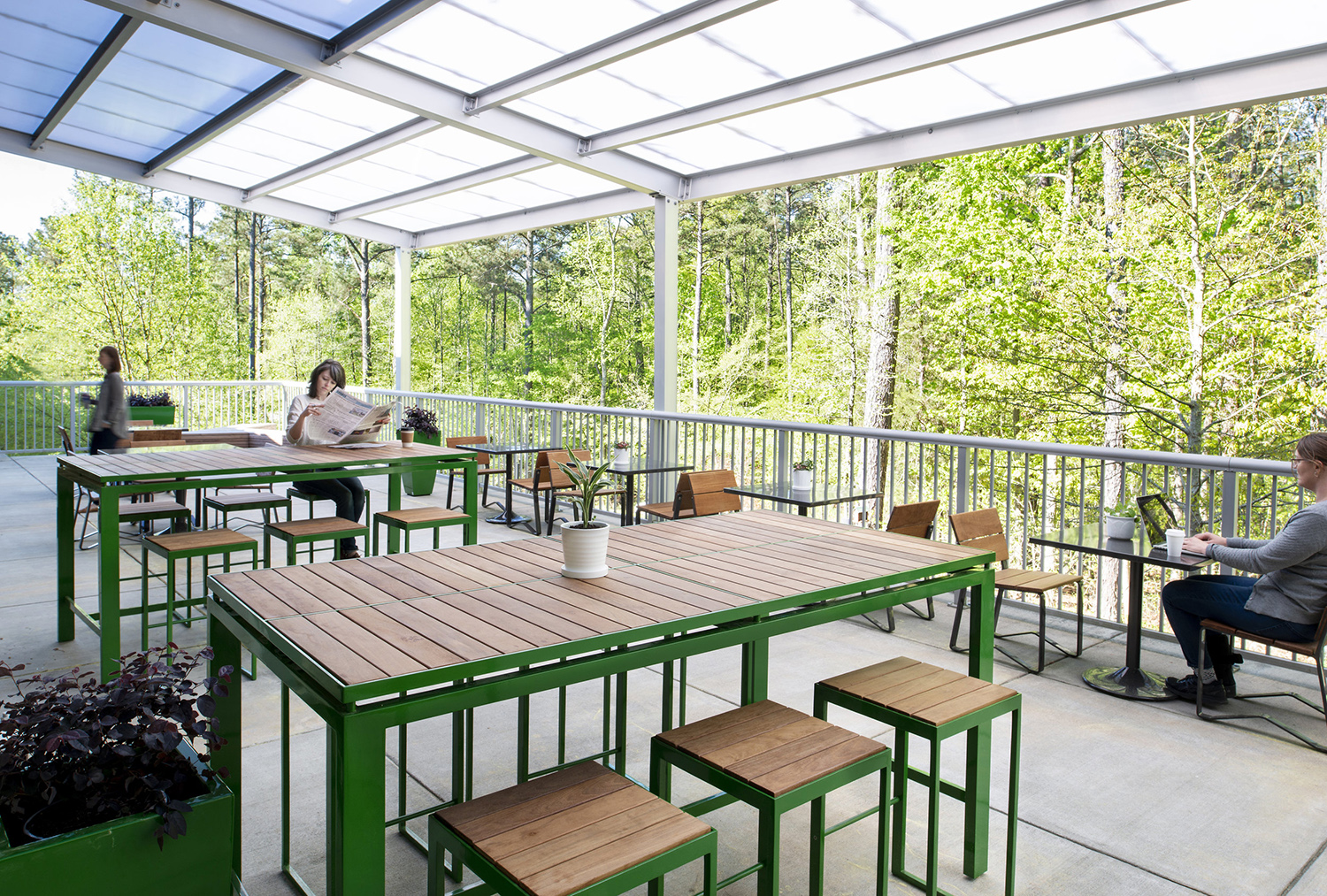 Patio area of the terrace showing wooden tables and seating with two patrons: one reading a newspapers and the other typing on a laptop