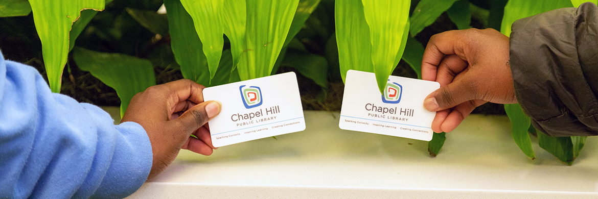 Image of two people's hands holding a Chapel Hill Public Library card