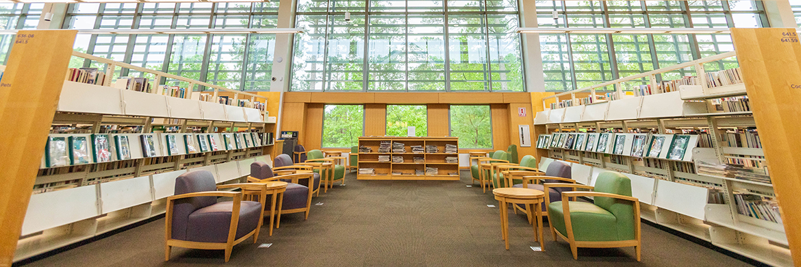 interior shot of the Reading Room in the Chapel Hill Public Library showing large windowed walls and rows of shelves with materials
